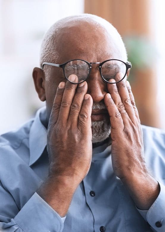 An elderly man wearing eyeglasses rubs his eye, possibly experiencing discomfort from glaucoma. Glaucoma treatment is available to help manage this condition.
