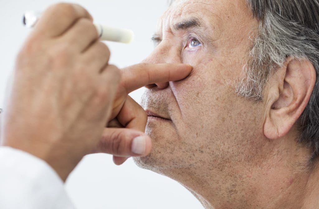 An ophthalmologist carefully examining the eye of an elderly man for signs of possible cataract recurrence.
