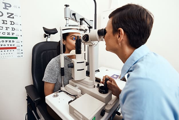 Optometrist examining a woman's eye with equipment, emphasizing Medicare coverage for eye exams.