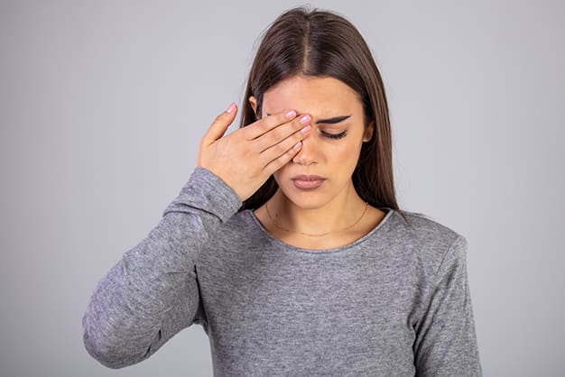 Young woman holding her hand over one eye, appearing uncomfortable, possibly experiencing blurry vision in one eye.